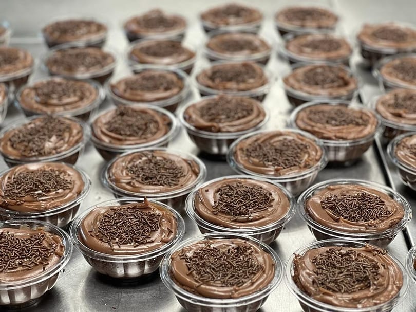 Rows of individual chocolate puddings with chocolate sprinkles in clear plastic cups.
